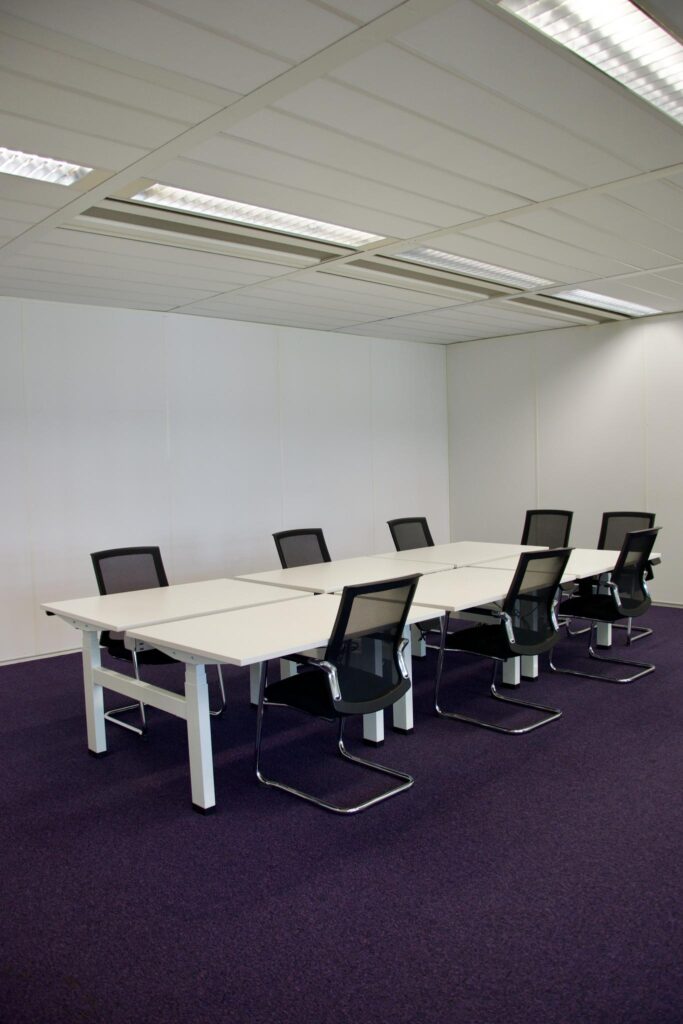 Modern meeting room with white tables, black mesh chairs, and purple carpet at Koningin Wilhelminaplein.